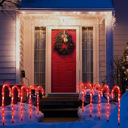 Solar-powered Christmas candy cane lights illuminating a snowy pathway in a festive outdoor setup.
